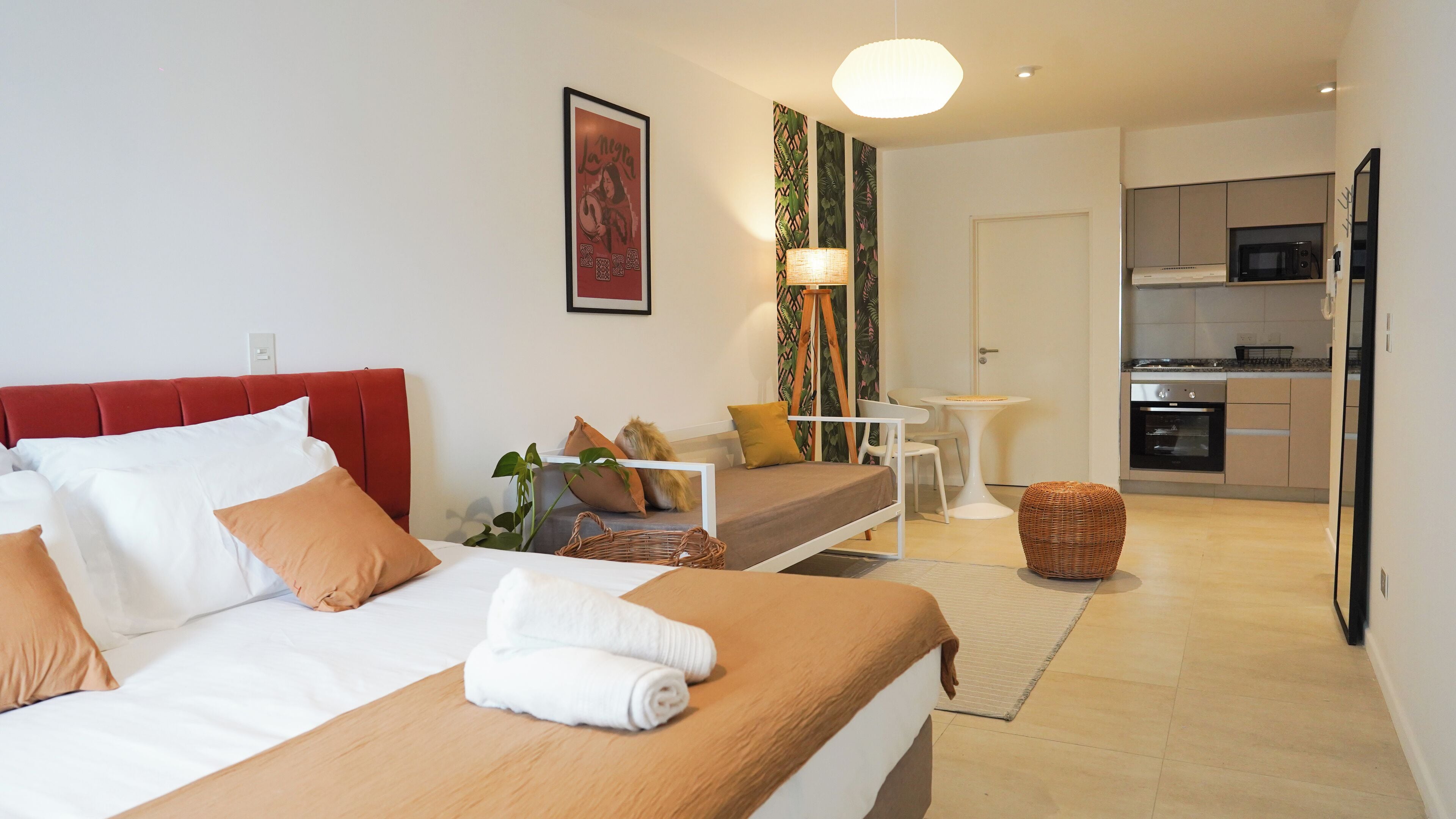 A hotel room with a bed, a sofa, a small table, a kitchen area, and a dining table.