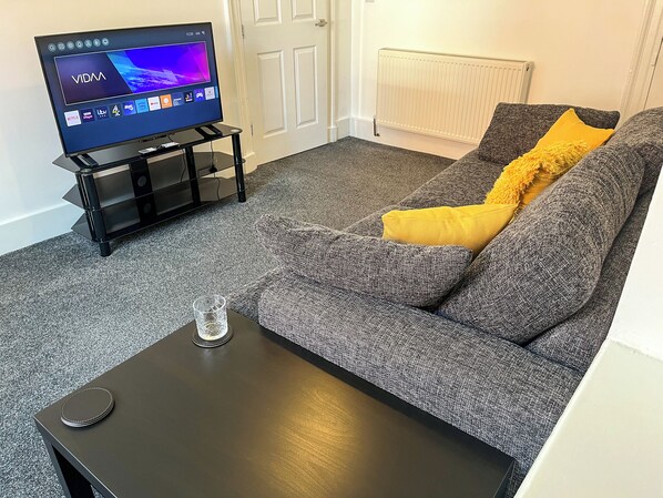 A living room with a grey sofa, a black coffee table, and a TV on a stand.