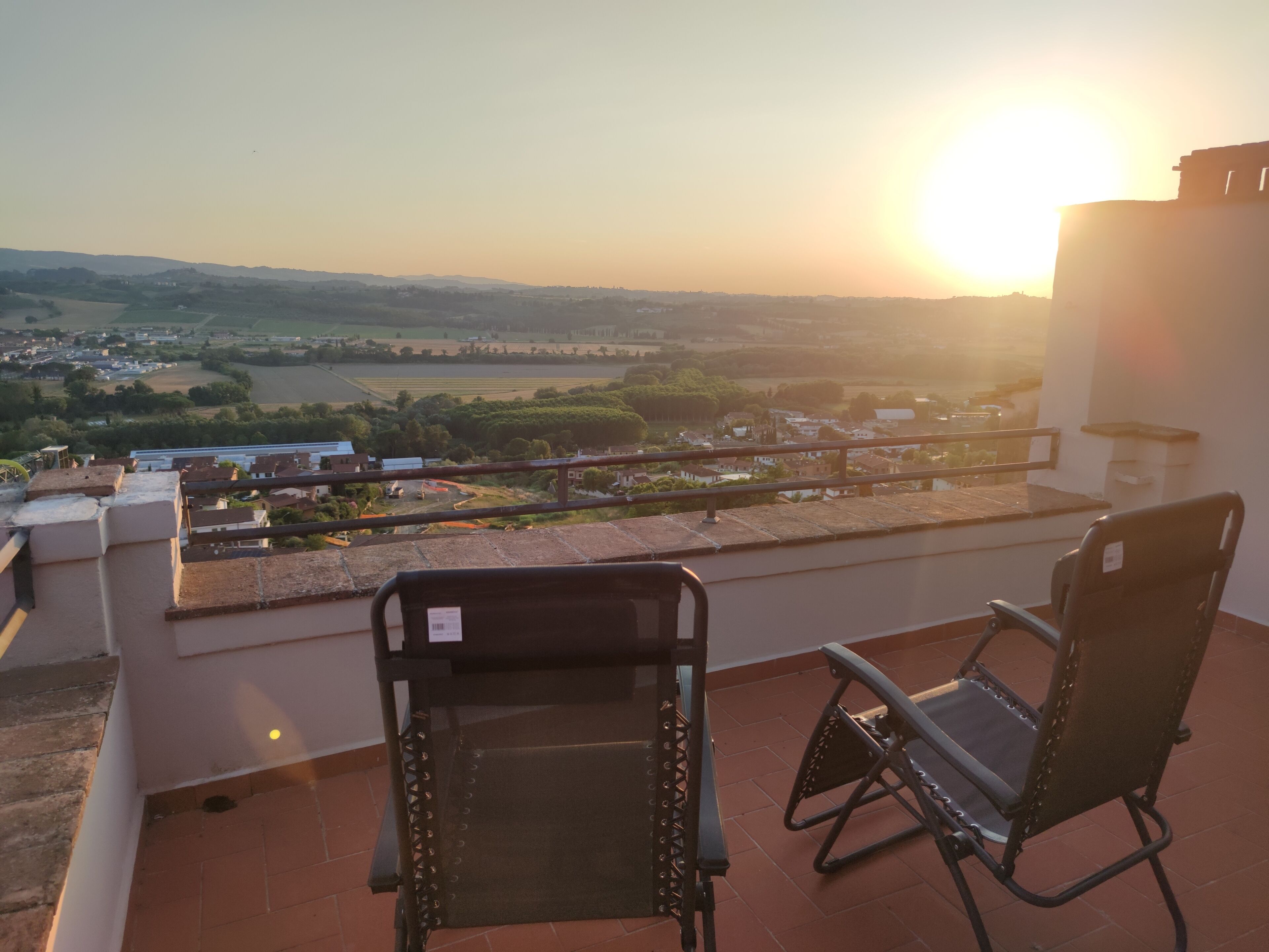 A terrace with two chairs overlooking a scenic view of a town and a river during sunset.