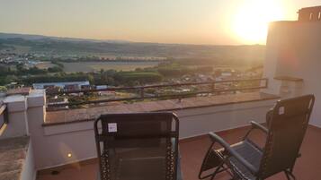 A terrace with two chairs overlooking a scenic view of a town and a river during sunset.