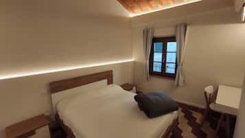 Quarto com cama, mesa de cabeceira e janela com cortinas.
