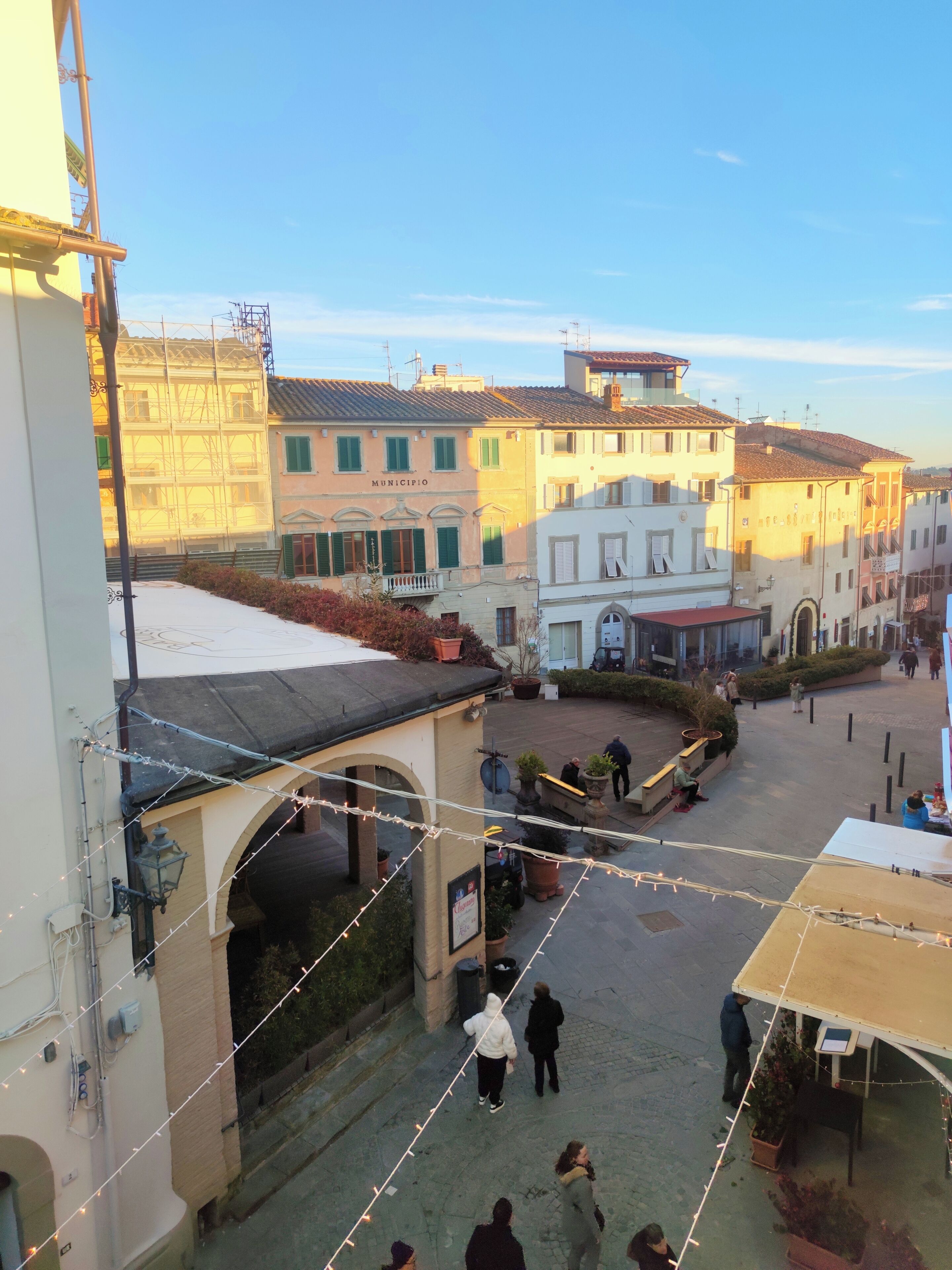 A courtyard with buildings, a covered seating area, and a street in the background.
