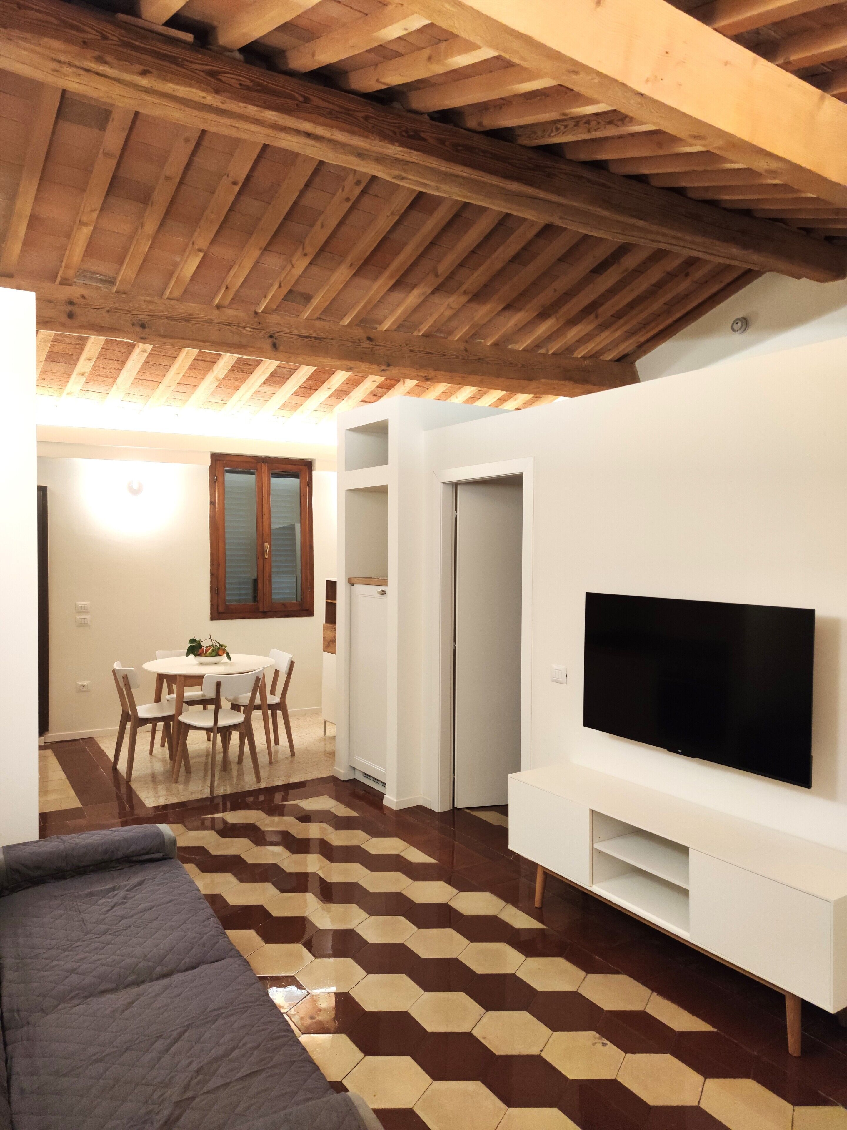 A modern living room with a flat-screen TV, a dining area with a table and chairs, and a patterned floor.