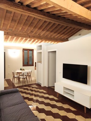 A modern living room with a flat-screen TV, a dining area with a table and chairs, and a patterned floor. - Apartment with a large panoramic terrace in the village center (Peccioli)