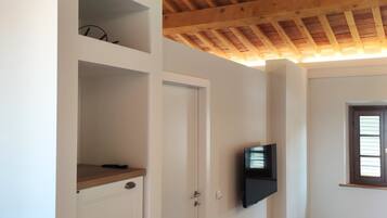 Una stanza con soffitto in legno, una porta bianca, una TV a schermo piatto montata al muro e un pavimento decorato.