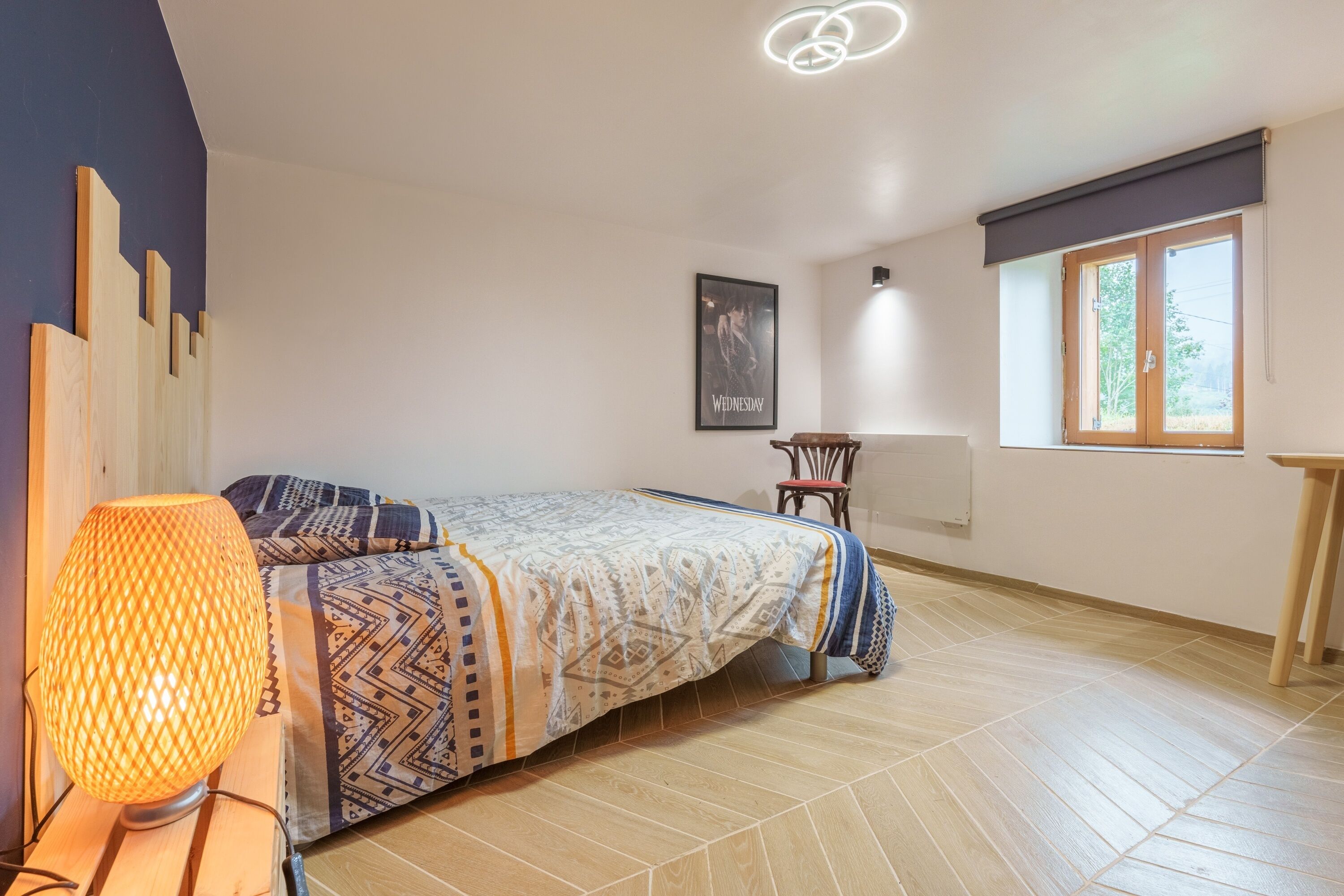 Een slaapkamer met een bed, een lamp, een stoel, een raam en een poster aan de muur.