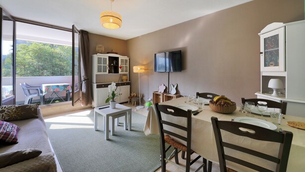A dining area with a table set for four, a sofa, a television, and a view of the outdoors.