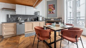 A modern kitchen with wooden cabinets, a black countertop, and a dining area with a table and chairs. - Fenêtre sur cour - Studio pour 2 (Lyon)