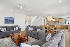 A modern living room with grey sofas, a wooden coffee table, and a dining area with wooden chairs and a glass-top table.