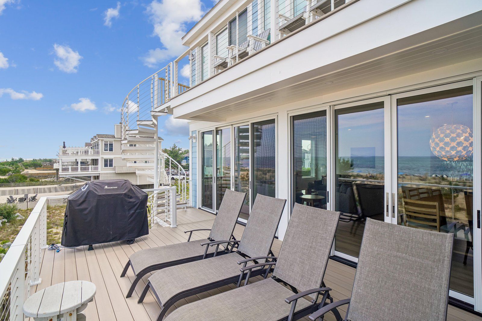 Een balkon met buitenmeubilair, een barbecue en uitzicht op zee en gebouwen.