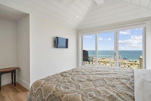 Un dormitorio con una cama grande, un televisor en la pared y vista a la playa.