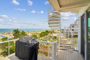 Ein Balkon mit Blick auf Strand und Meer, ein überdachter Grill und eine Wendeltreppe.