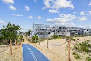 Una propiedad frente al mar con un paseo arenoso que conduce a varias casas modernas con grandes ventanales y balcones.