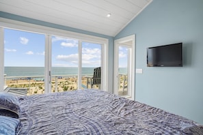 Un dormitorio con una cama grande, un televisor montado en la pared y vistas a la playa.