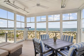 A covered outdoor seating area with a table and chairs, a telescope, and a view of the beach.