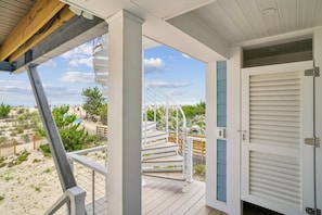 Un espacio al aire libre cubierto con una terraza de madera, una escalera espiral y vistas a la playa.
