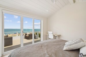 Dormitorio con cama grande, escritorio y silla, con vista a la playa.