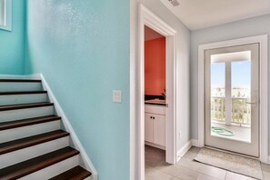 A staircase leading to a room with a view of the beach, a door to a kitchen, and a balcony with a railing.