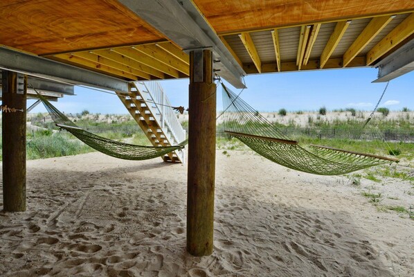 A beach scene with two hammocks under a wooden structure, a staircase, and a sandy beach with vegetation.