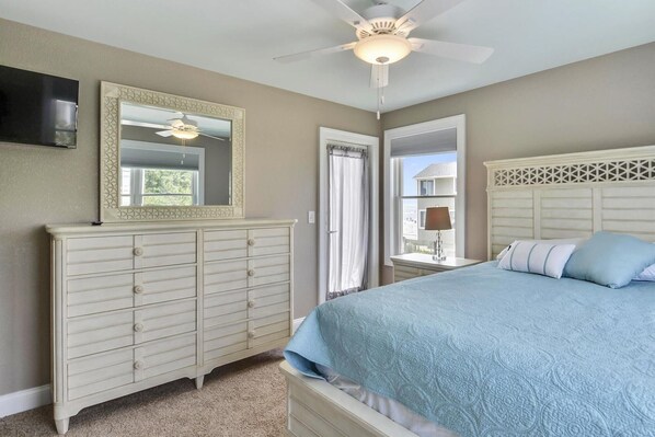 Une chambre à coucher comprenant un lit, une commode, un ventilateur de plafond et deux fenêtres.