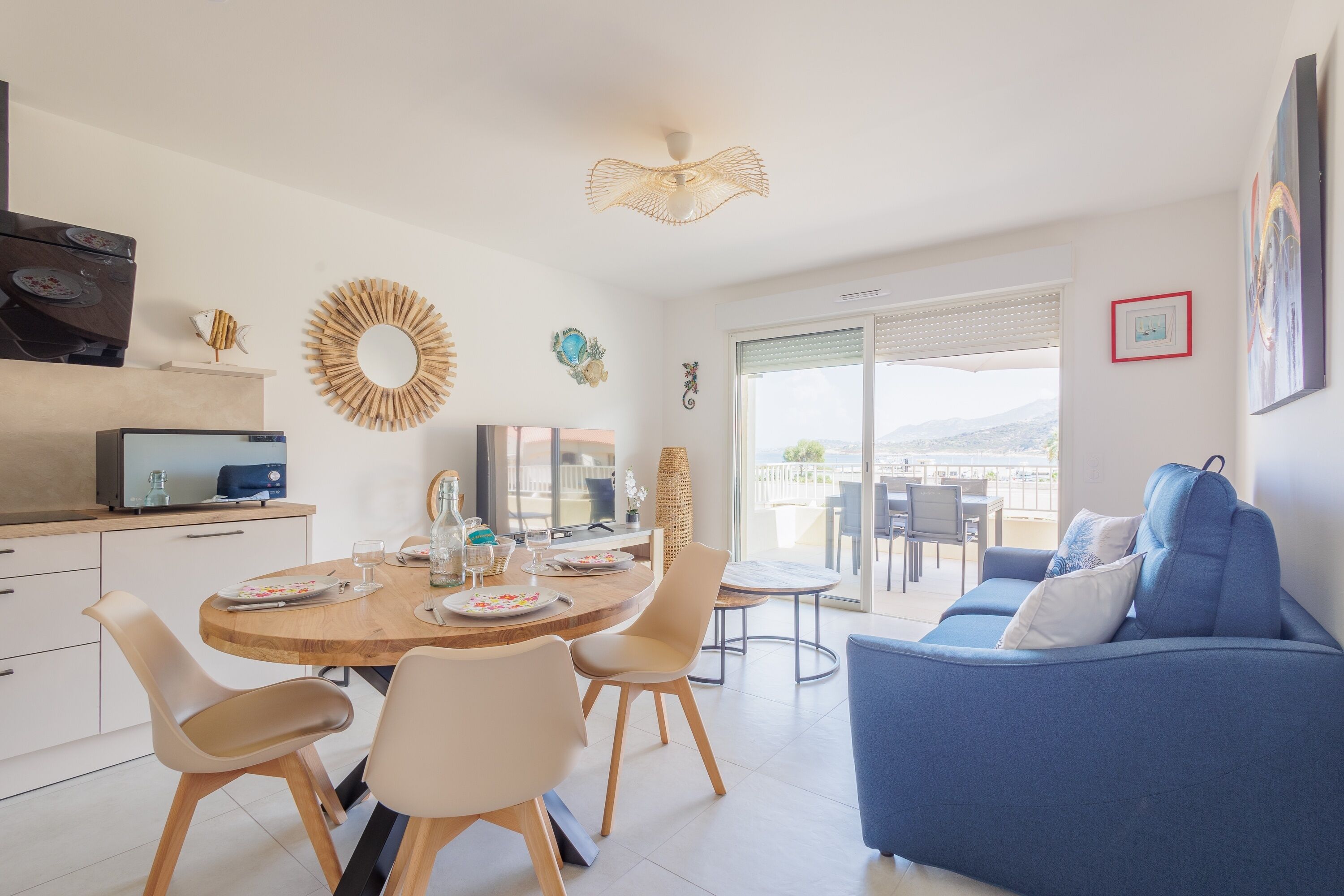 Een moderne woonkamer met een blauwe bank, een eethoek met een houten tafel en stoelen, en een keuken met een televisie en kasten.