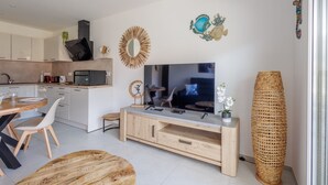 Una cuina moderna amb un televisor gran, armaris de fusta i zona de menjador amb una taula rodona i cadires.
