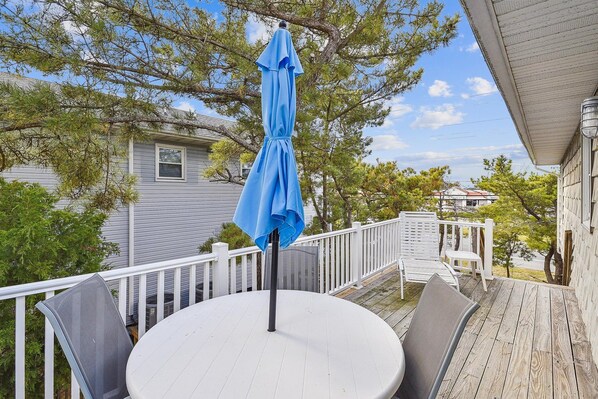 Une table ronde avec un parasol bleu, des chaises blanches et une balustrade blanche sur une terrasse en bois.