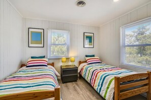 Quarto com duas camas, uma mesa de cabeceira e quadros nas paredes.