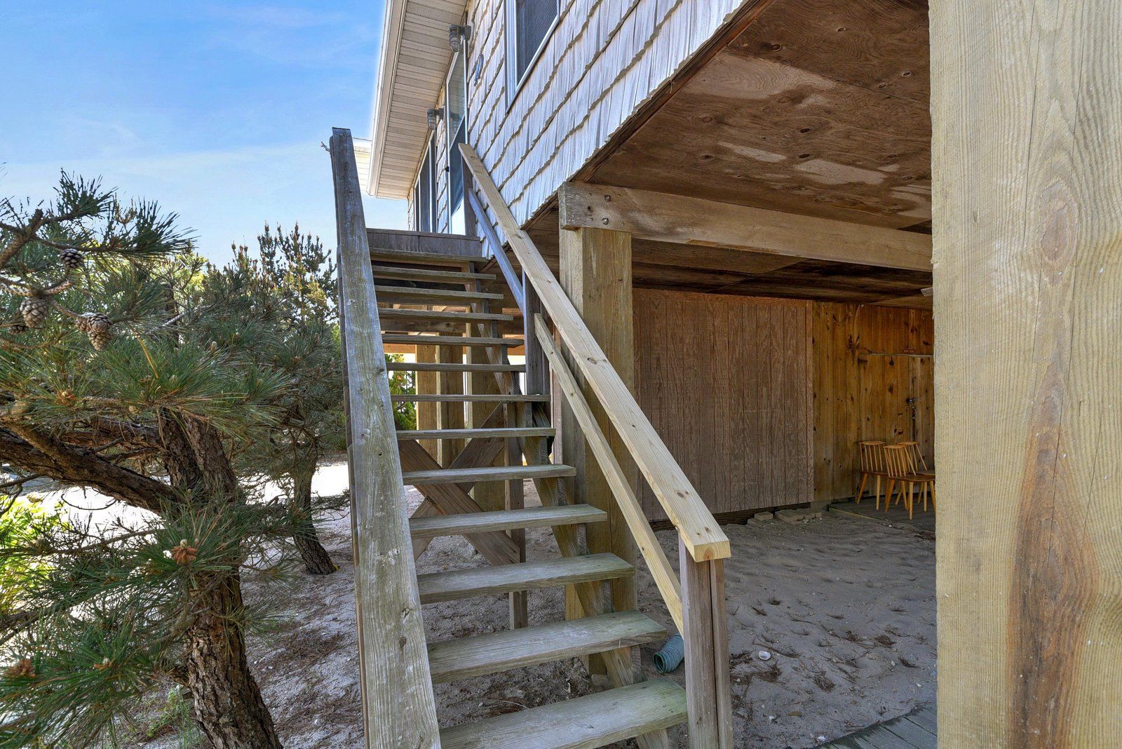 A wooden staircase leading to a covered outdoor area with a sandy ground.