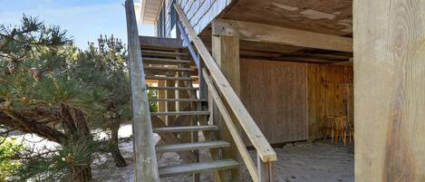 A wooden staircase leading to a covered outdoor area with a sandy ground.