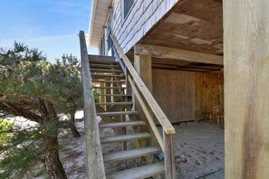A wooden staircase leading to a covered outdoor area with a sandy ground.