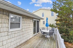 A covered patio with a table and chairs, a blue umbrella, and a wooden deck. - Pet Friendly Oceanside Getaway in Bethany Beach! (South Bethany)