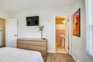 A bedroom with a bed, a dresser, a television, and a bathroom visible through an open door. - Pet Friendly Oceanside Getaway in Bethany Beach! (South Bethany)