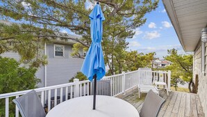 A covered outdoor deck with a round table and chairs, a blue umbrella, and a view of neighboring houses. - Pet Friendly Oceanside Getaway in Bethany Beach! (South Bethany)