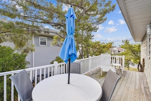 A covered outdoor deck with a round table and chairs, a blue umbrella, and a view of neighboring houses. - Pet Friendly Oceanside Getaway in Bethany Beach! (South Bethany)