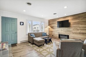 A living room with a sofa, a coffee table, a TV mounted on a wooden wall, and a fireplace.