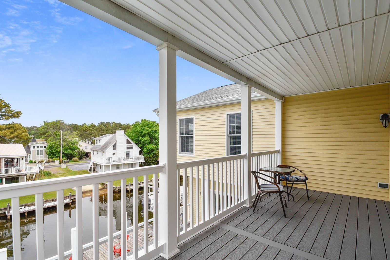 A covered porch with a view of a residential area, a small table with chairs, and a lamp post.