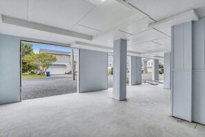 Un espace intérieur avec des piliers en béton, un sol en béton et une vue sur l’extérieur par une porte ouverte.
