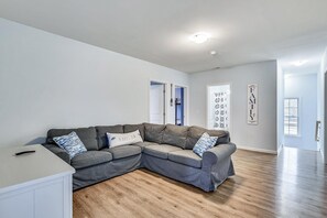 Uma sala de estar moderna com um sofá seccional cinza, um armário branco e piso de madeira.