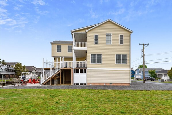 A two-story building with a balcony on the second floor, a covered entryway, and a visible garage door. - 7 Bedroom Bayside Home in Bethany Beach: Elevator, Pool, Short Walk to Beach! (South Bethany)