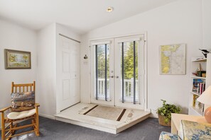 Una habitación con una puerta blanca, una silla de madera con cojín, una estantería y un mapa en la pared.