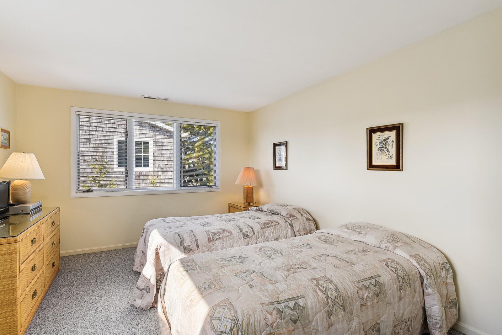 A bedroom with two beds, a dresser, a window with blinds, and two wall-mounted lamps.
