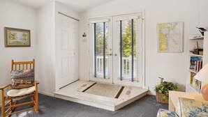 Een kamer met een houten stoel, een witte deur, een kaart aan de muur en een boekenplank.