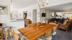 Een ruime woonkamer met een houten eettafel, rieten meubels en een moderne kroonluchter.