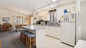 Een moderne keuken met een centraal eiland, witte kasten, een koelkast en barstoelen.
