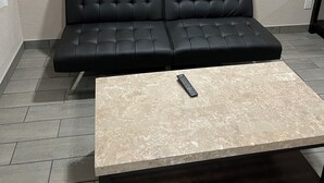 A black leather sofa against a textured wall, a remote control on a marble-topped coffee table, and a wall-mounted light fixture.