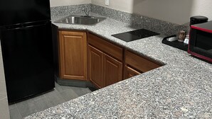 A kitchen with granite countertops, wooden cabinets, a stainless steel sink, and a black refrigerator.