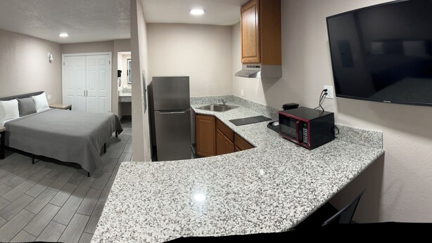 A compact hotel room with a bed, a small sofa, a kitchenette, and a TV.