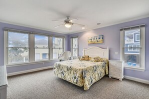 A bedroom with a bed, a ceiling fan, and large windows.