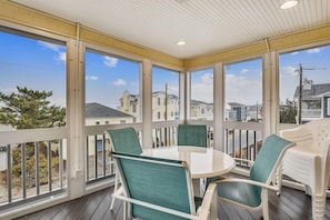 A covered patio with a table and chairs, large windows, and a view of neighboring houses.